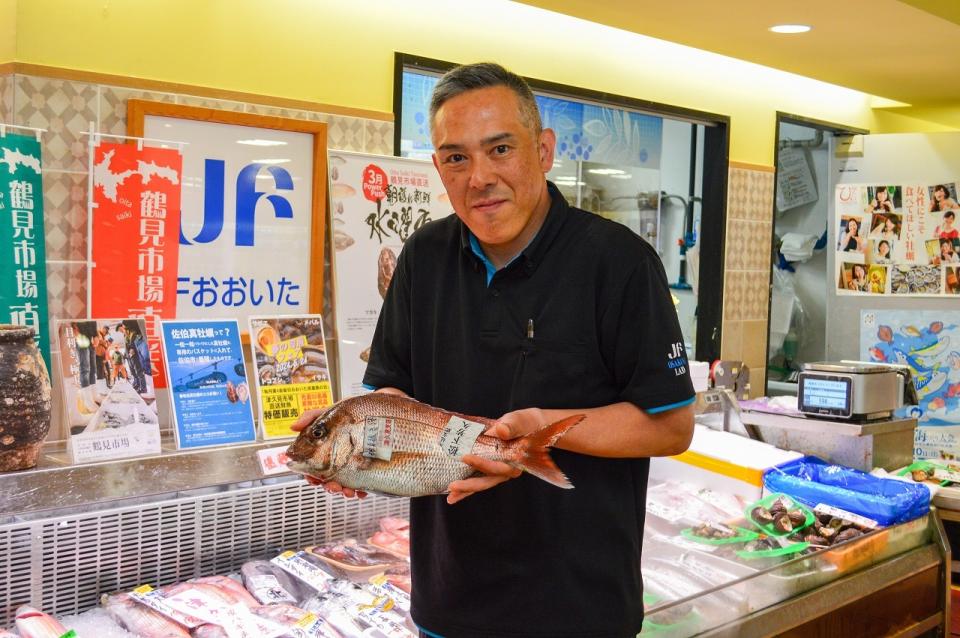 店の前で魚を両手で一尾持って見せる店主